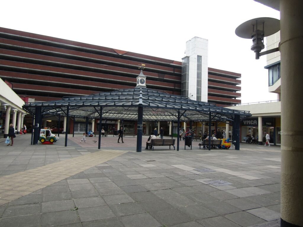 Anglia Square shopping centre in Norwich in 2019, with its glass canopy and clock in front of the Sovereign House multi-storey car park