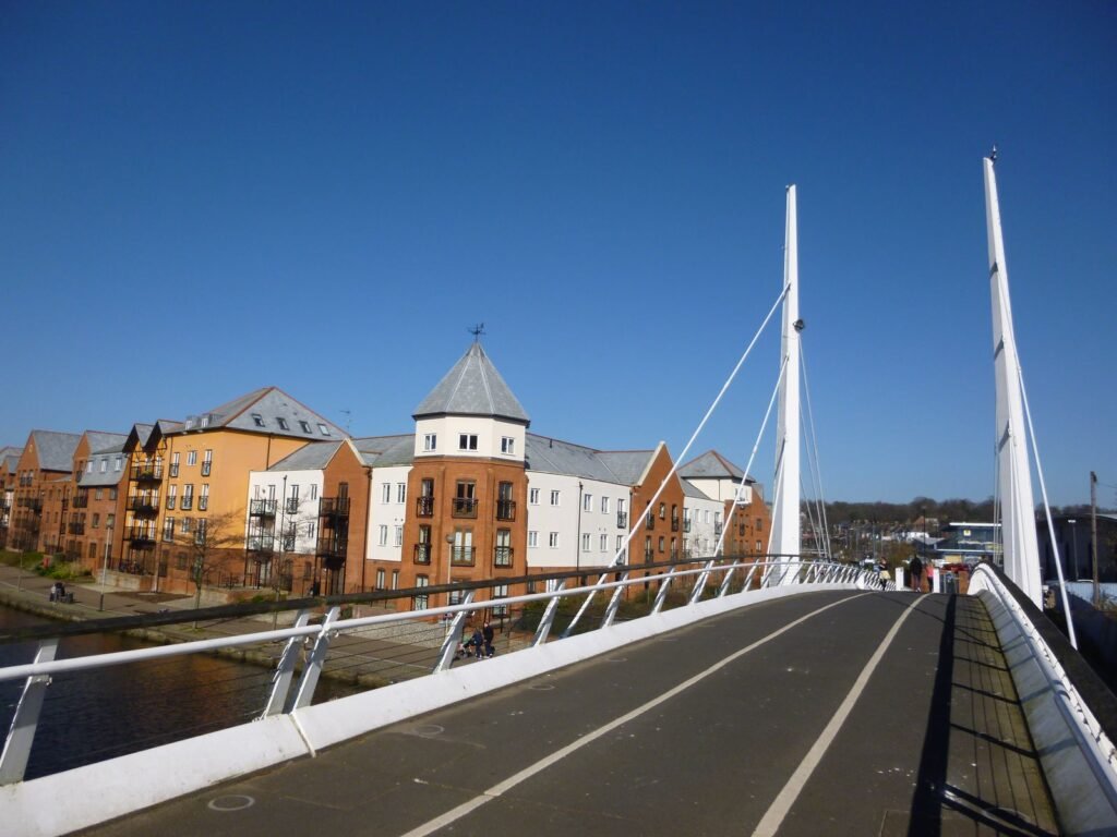 Modern apartment blocks beside the River Wensum in Norwich, seen from a white cable-stayed footbridge