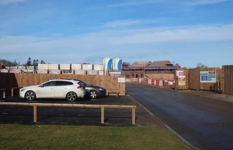 Houses under construction behind hoarding at the Prince's Park development, New Rackheath, February 2023